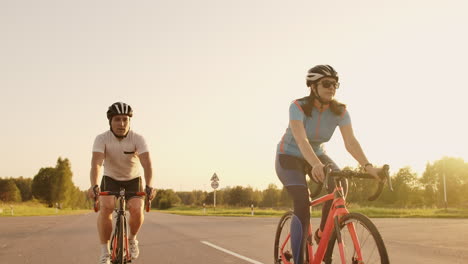 Steadicam-shot-of-two-healthy-mem-and-woman-peddling-fast-with-cycling-road-bicycle-at-sunset